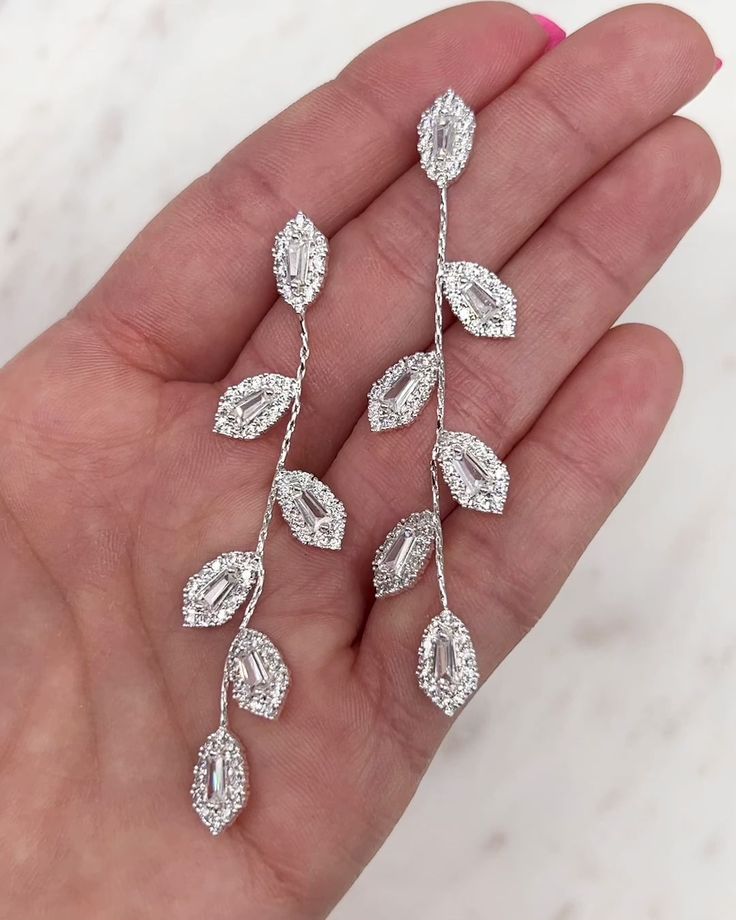 a woman's hand is holding three pairs of earrings with leaves and diamonds on them