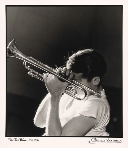 a woman holding a trumpet in her right hand and wearing a white shirt with writing on it