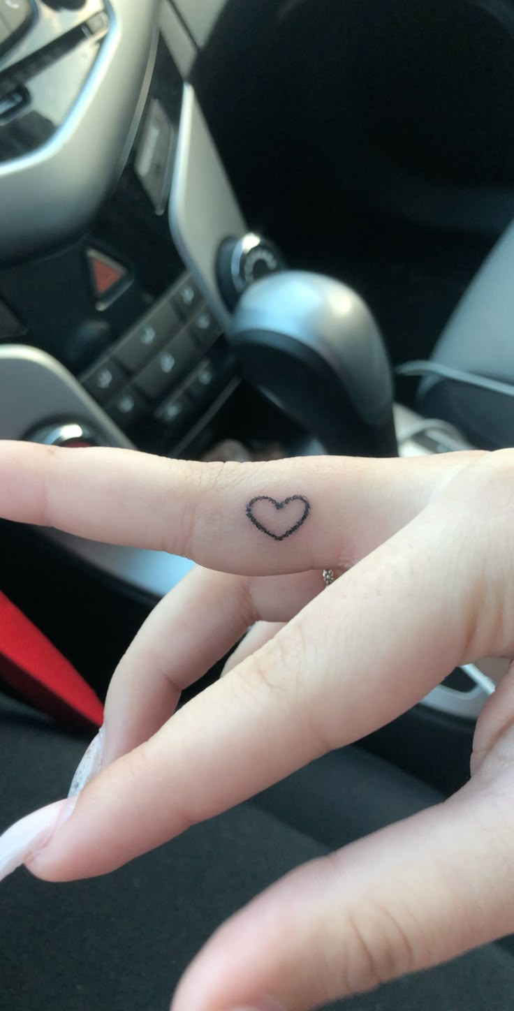 a person's finger with a heart tattoo on it and a car steering wheel in the background