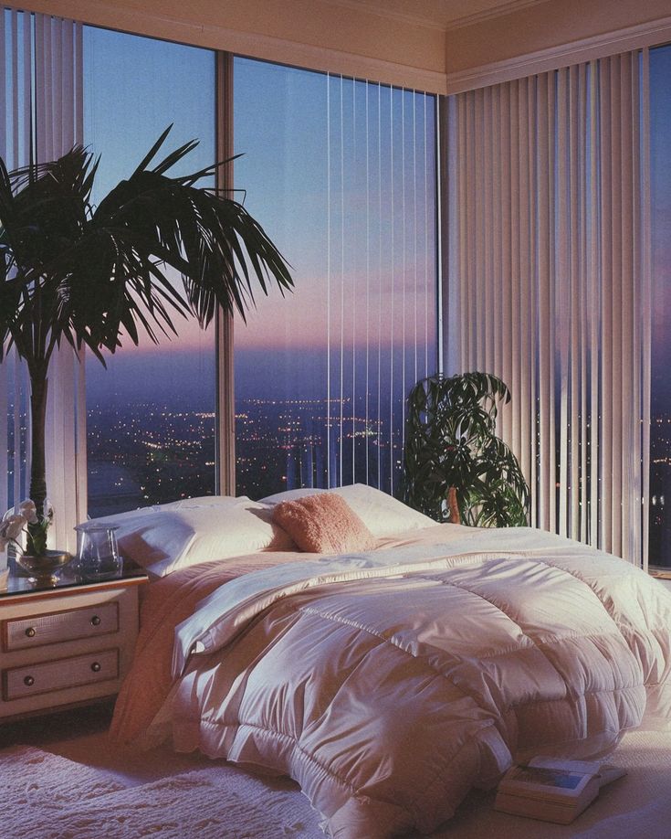 a bedroom with a large window overlooking the city at night and palm tree in the corner