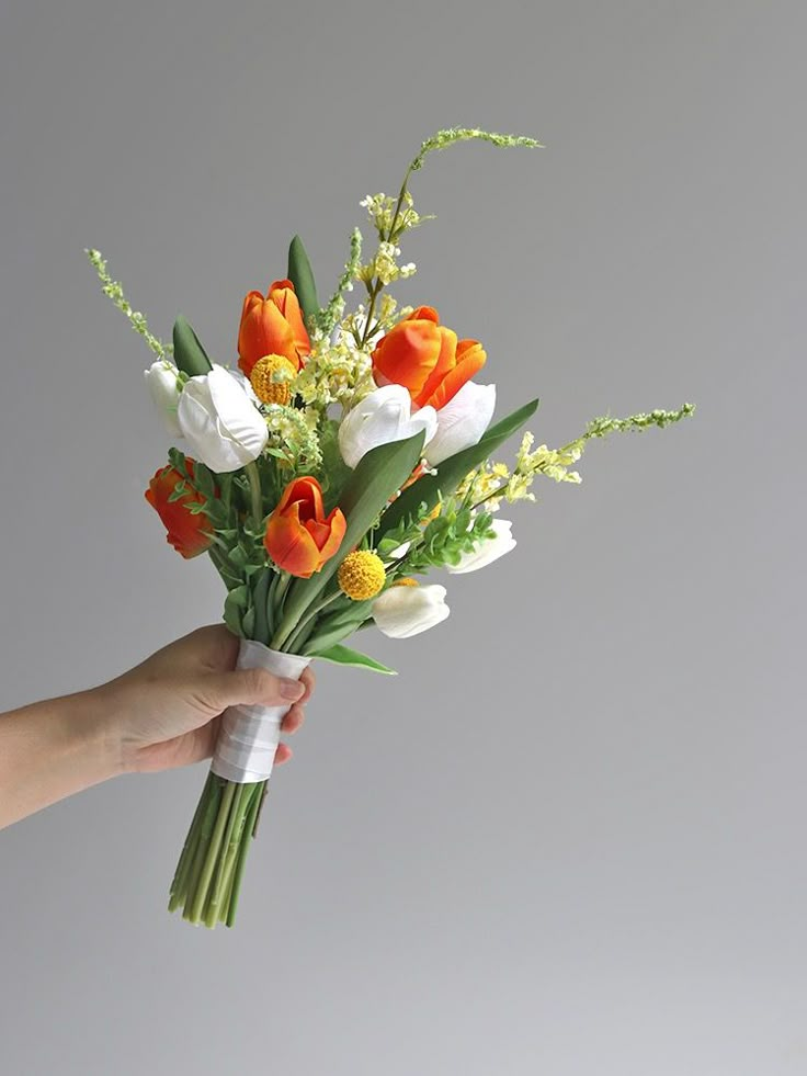 a hand holding a bouquet of flowers on a gray background in front of a white wall