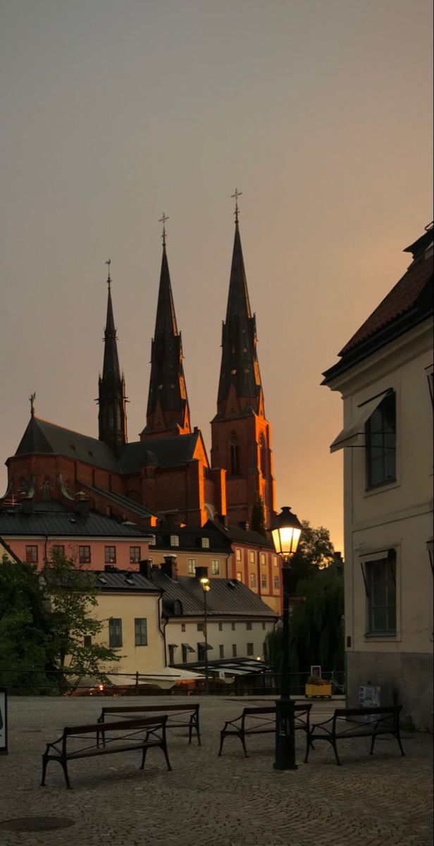 the sun is setting over an old town with benches and buildings in front of it