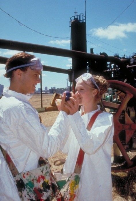 a man and woman standing next to each other in front of an industrial area with machinery