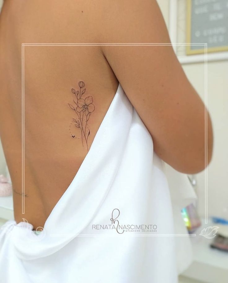 the back of a woman's white dress with a flower tattoo on her left shoulder