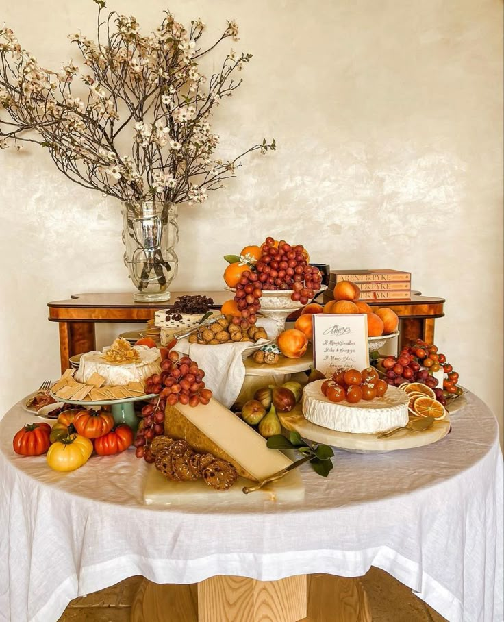 a table topped with lots of different types of cheeses and fruit next to a vase filled with flowers