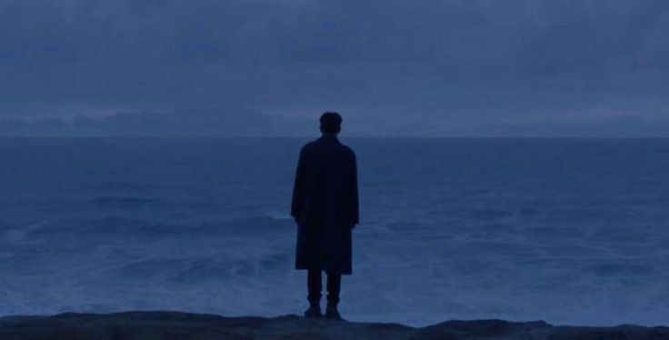 a man standing on top of a cliff next to the ocean