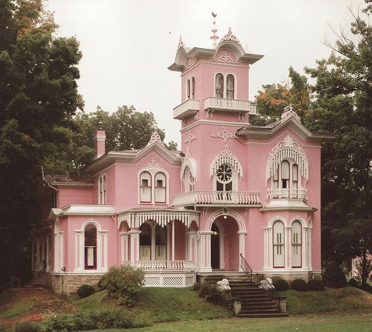 a pink house with white trim on the front and side windows, surrounded by trees