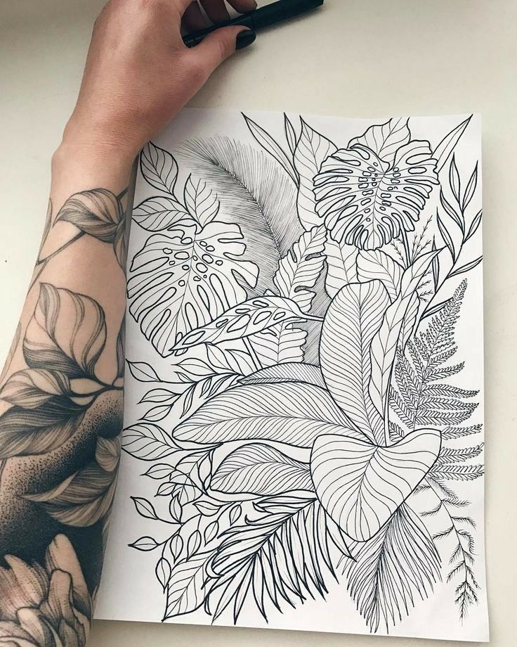 a person holding a pen over a drawing with flowers and leaves on the paper in front of them