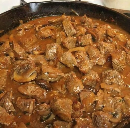 a skillet with meat and mushrooms cooking on the stove top, ready to be eaten