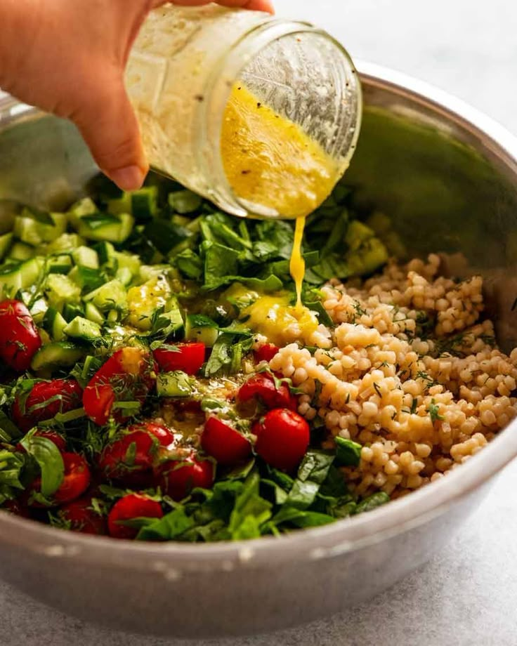 someone pouring dressing into a bowl filled with vegetables and grains, ready to be cooked