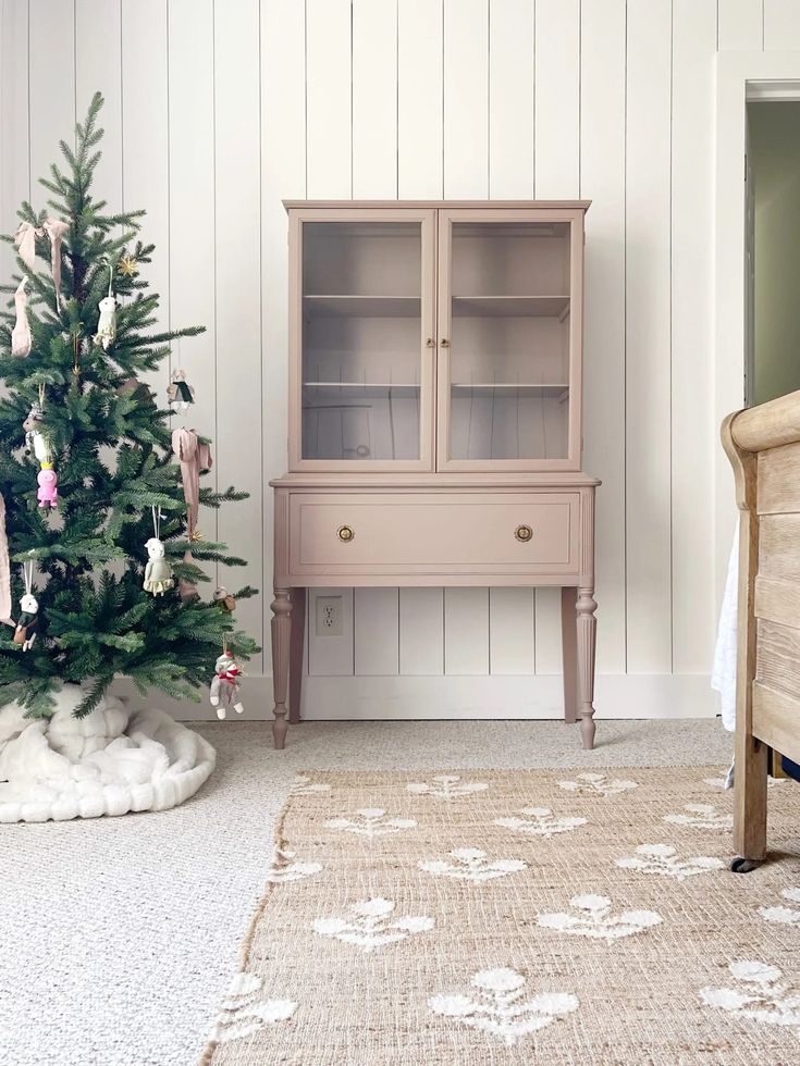 a small christmas tree sitting in front of a pink hutch next to a bed