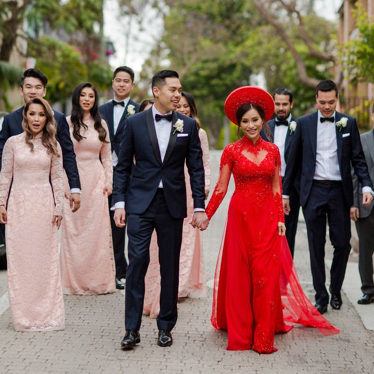 a group of people in formal wear walking down the street with one woman wearing a red dress