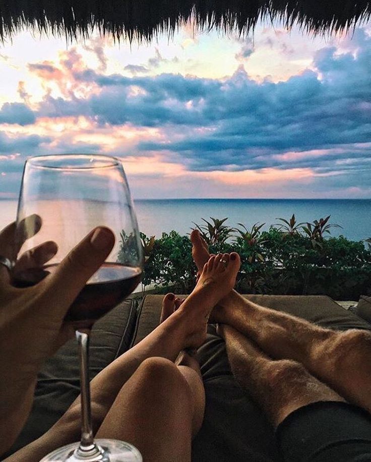 two people sitting on a couch with their feet propped up next to a glass of wine