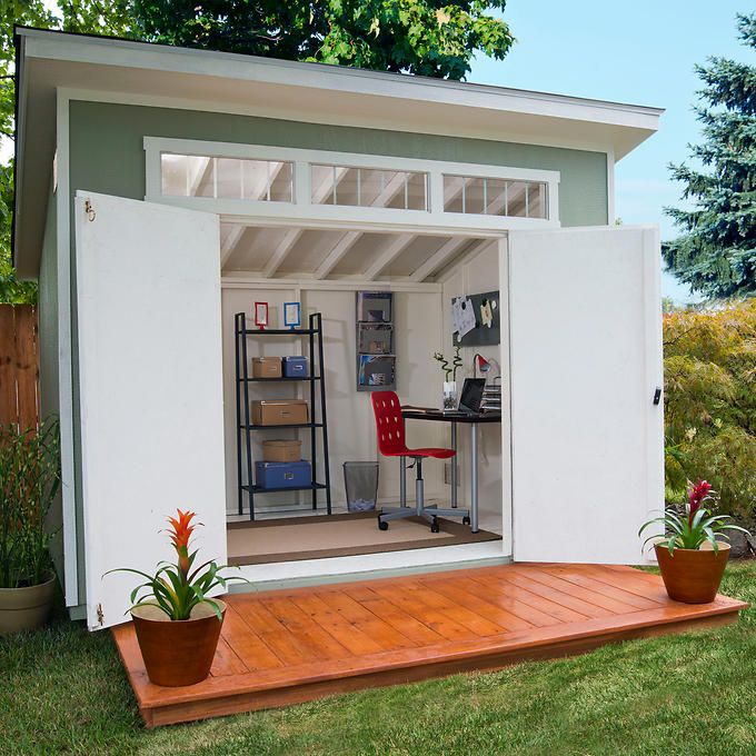 a small shed with a desk and chair in the back yard, surrounded by grass