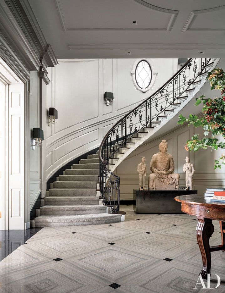 there is a statue in the middle of this room next to stairs and a clock on the wall