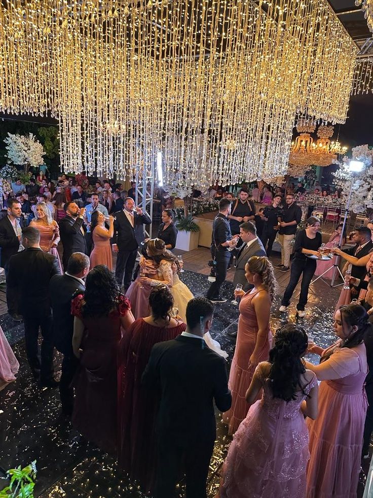 a group of people standing around in front of a stage with lights hanging from the ceiling