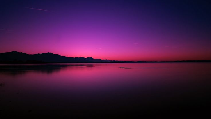 the sky is purple and pink as the sun goes down over mountains in the distance