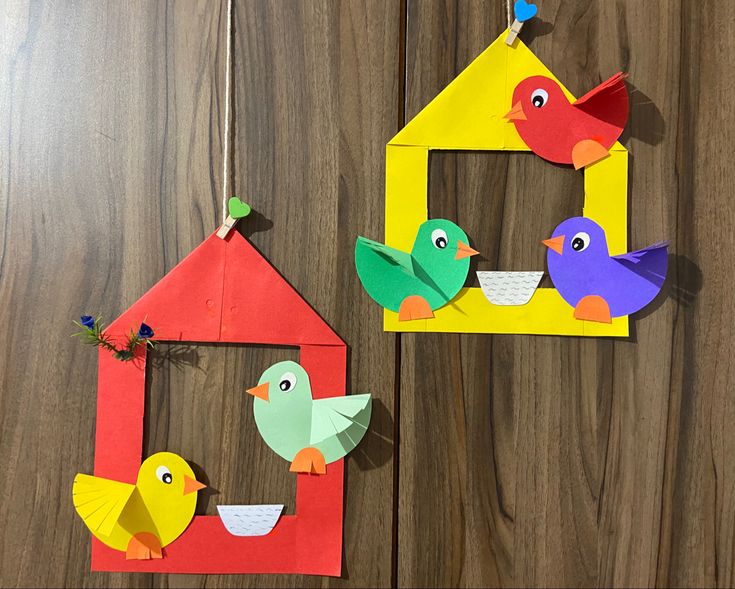 three colorful paper birds are hanging on the wall next to a house and bird feeder