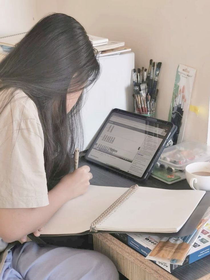 a woman sitting at a desk writing on a notebook