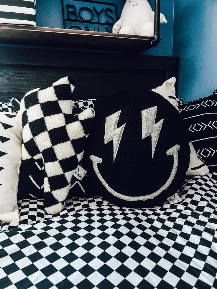 a black and white bed topped with lots of pillows next to a shelf filled with stuffed animals