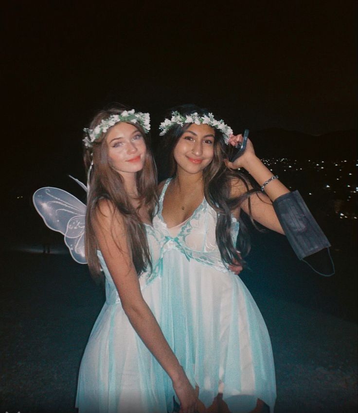 two women dressed in fairy costumes pose for a photo together at night with their arms around each other