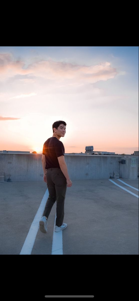 a man standing in an empty parking lot with the sun setting behind him and he is looking up