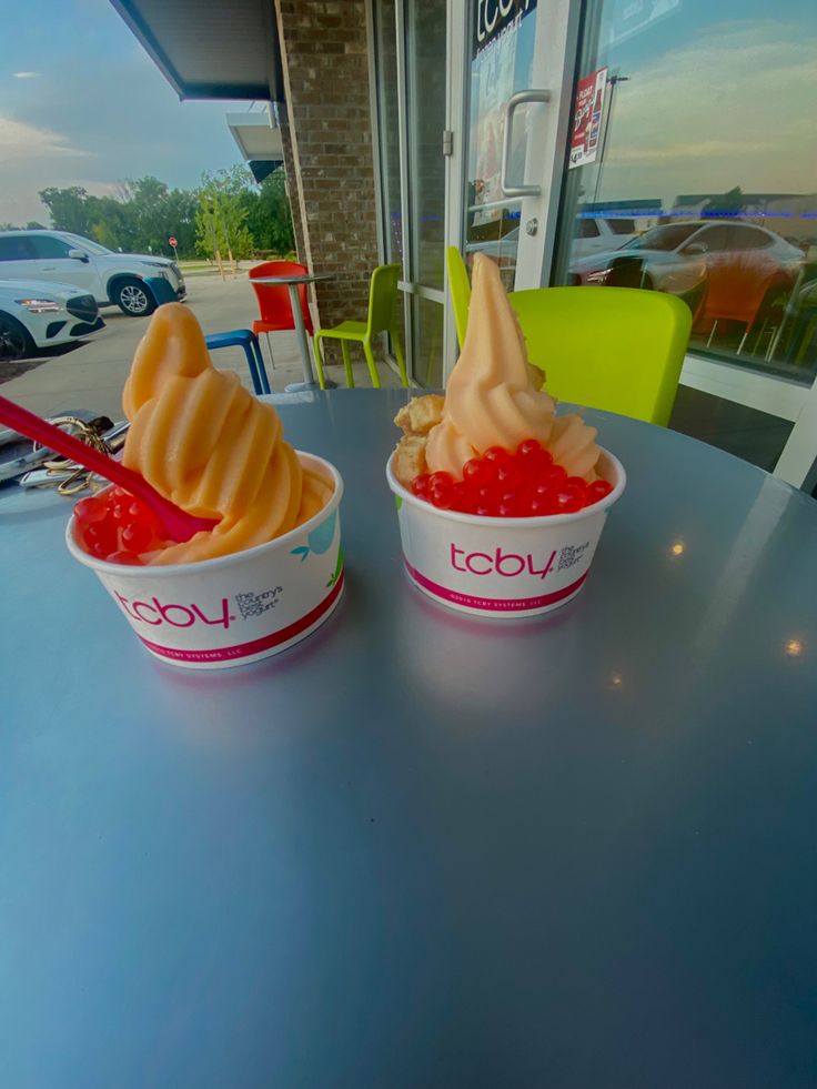 two ice cream cups with toppings in them on a table outside a storefront