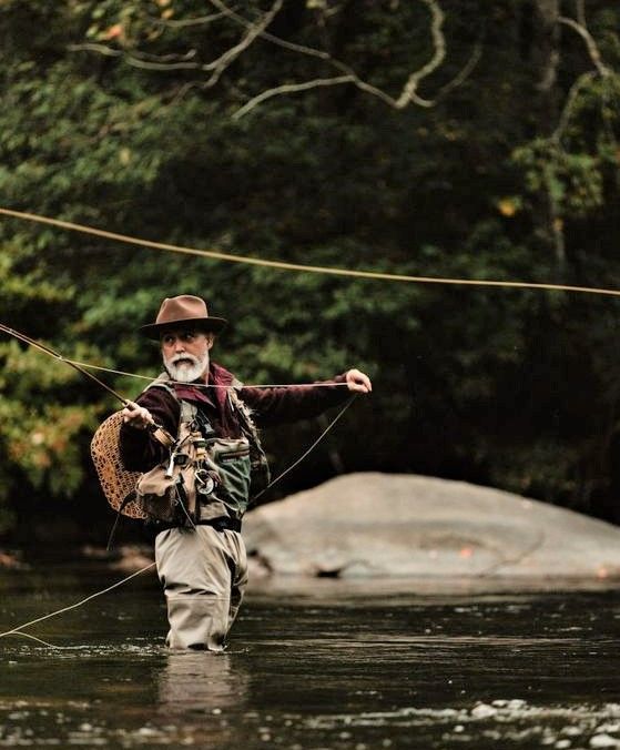 an older man is standing in the water holding a fishing rod and wearing a hat