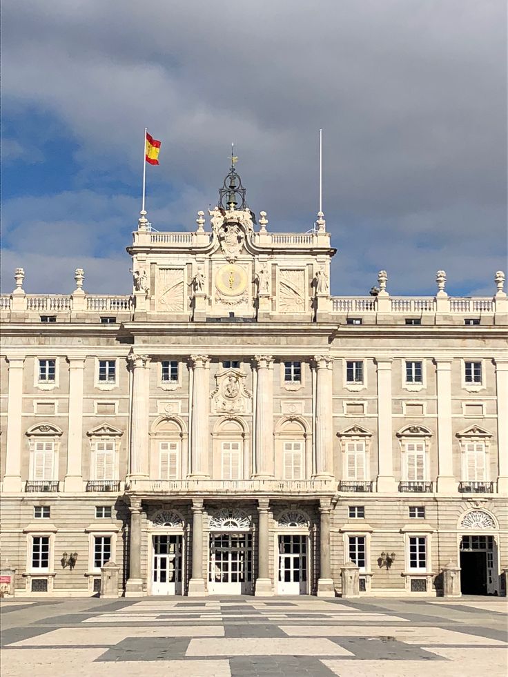 a large building with a flag on top of it's roof and two flags flying in the air