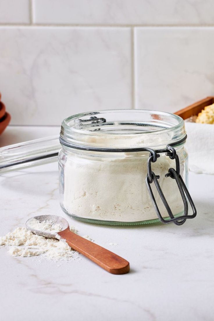 a glass jar filled with white powder next to a wooden spoon on a counter top