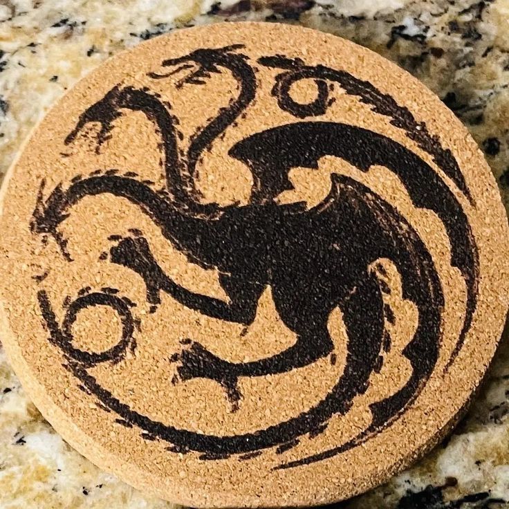 a black and white image of a dragon on a cork coaster sitting on a marble surface