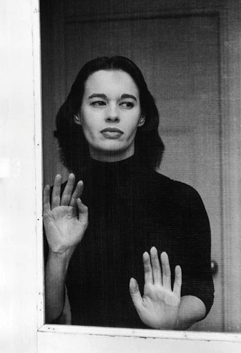 a black and white photo of a woman holding her hands up in front of the window