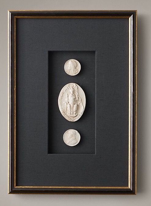 two framed coins are on display in a black and gold frame against a gray wall