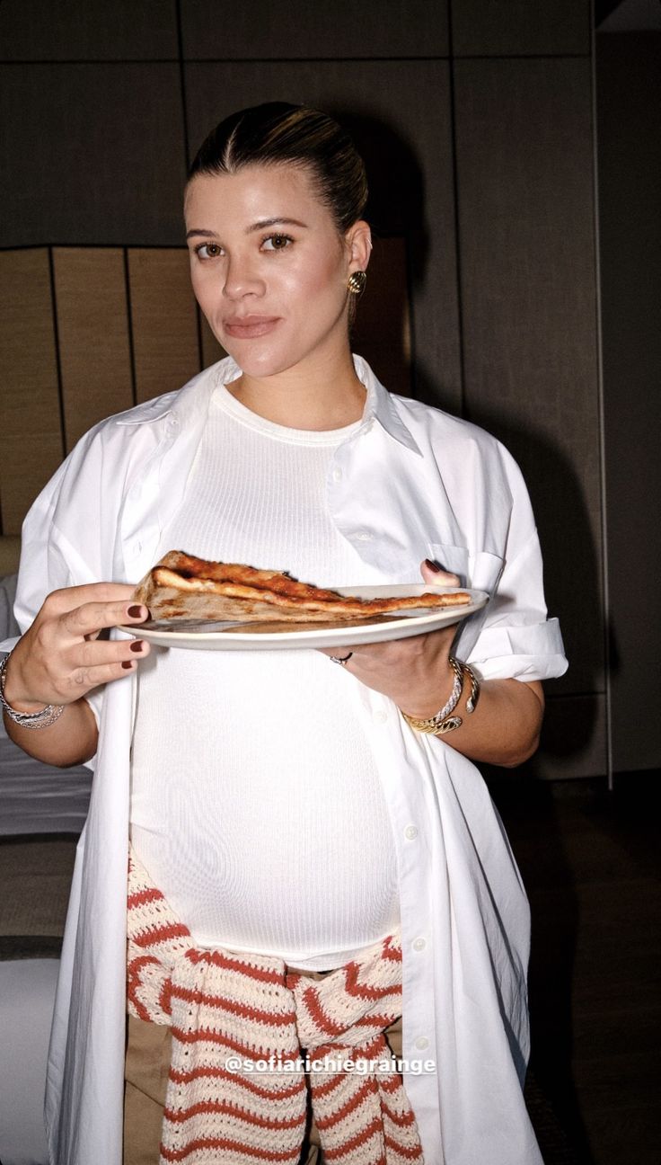 a pregnant woman holding a plate with pizza on it