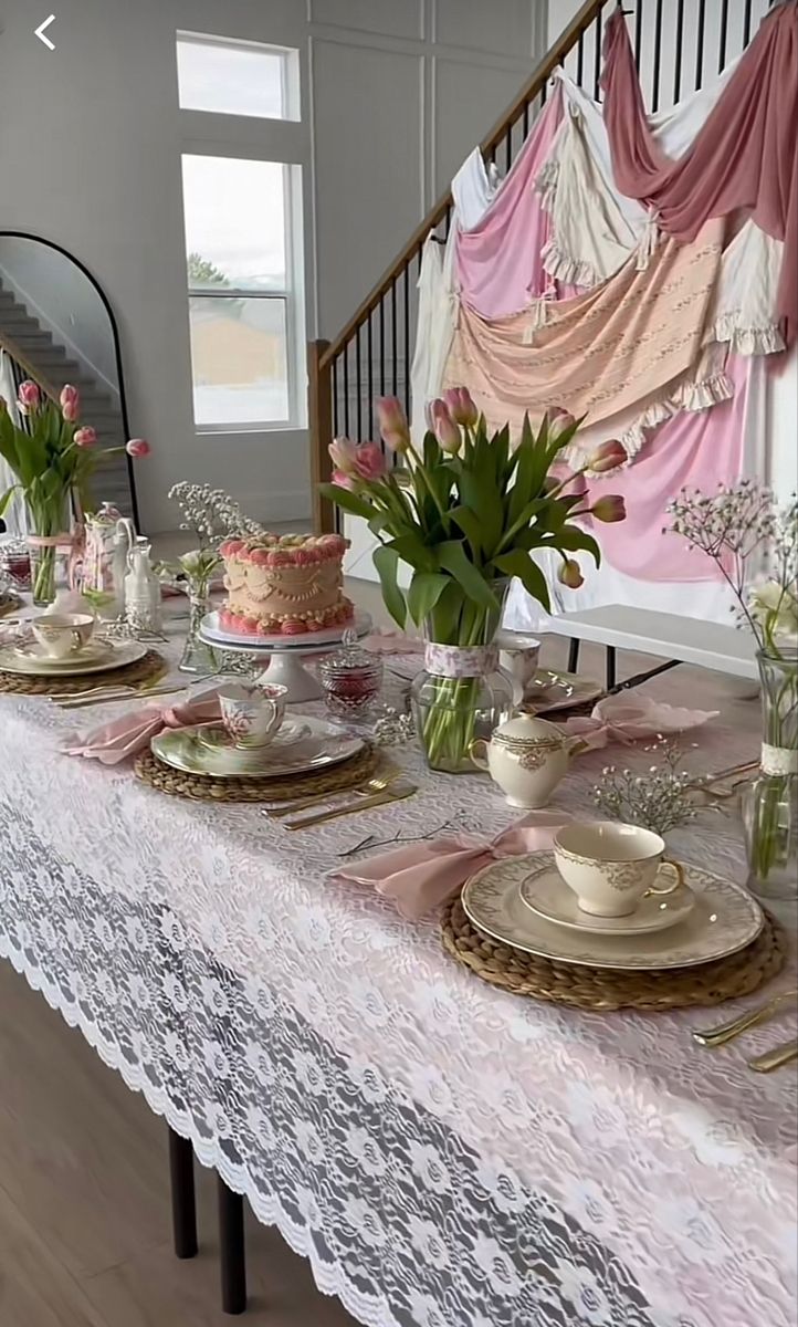 a long table is set with pink and white flowers in vases, plates and cups