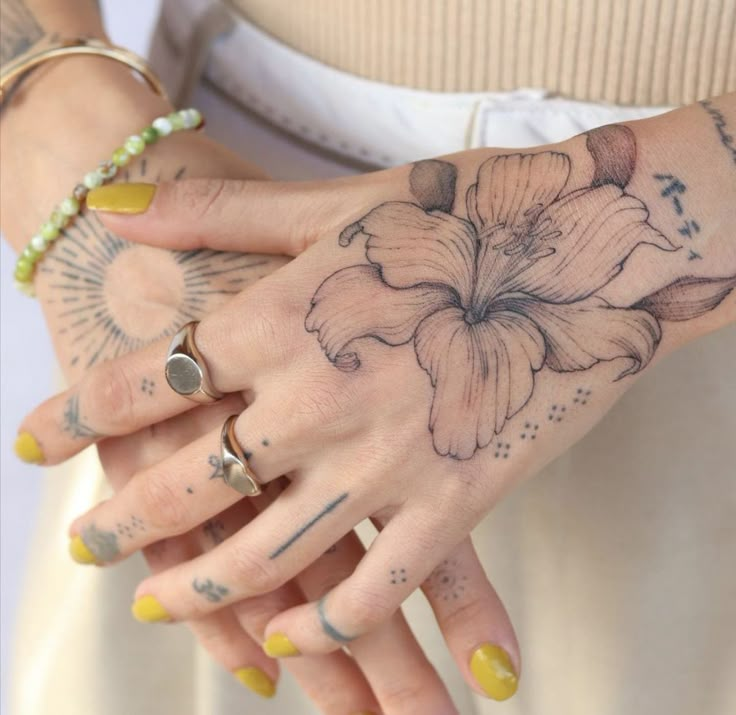 a woman's hands with tattoos and rings on her left wrist holding a flower