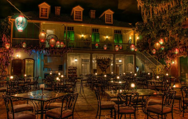 an outdoor dining area with tables and chairs lit up at night in front of a building