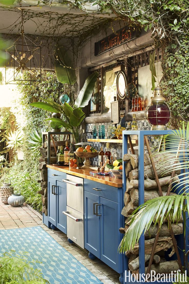 an outdoor kitchen with blue cabinets and lots of greenery on the walls, along with potted plants