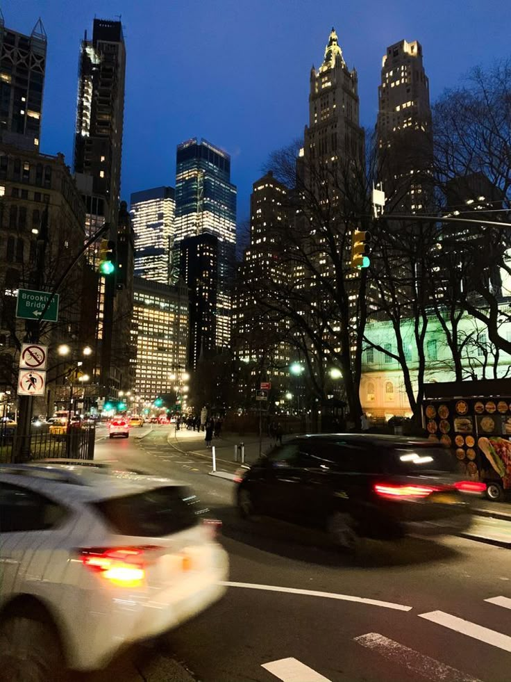 some cars are driving down the street in front of tall buildings at night with lights on