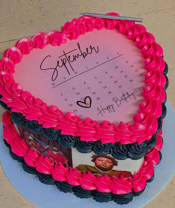 a pink and black heart shaped birthday cake on a blue plate with a note attached to it