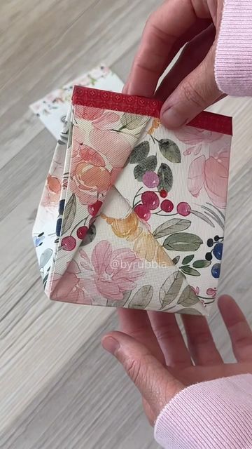 someone is holding an origami box with flowers on it and red ribbon around the top