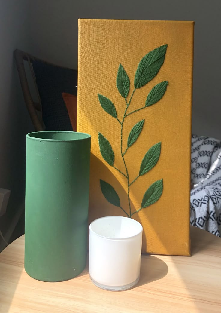 a green vase sitting on top of a wooden table next to a candle holder and painting