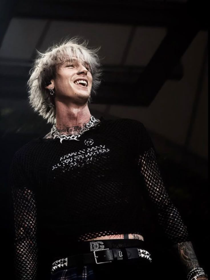 a man with blonde hair and piercings standing in front of a black background smiling