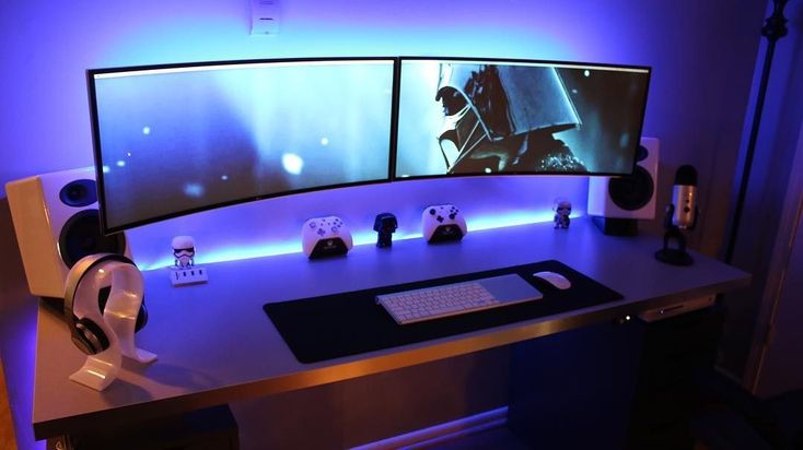 two computer monitors sitting on top of a desk with headphones and other items next to them