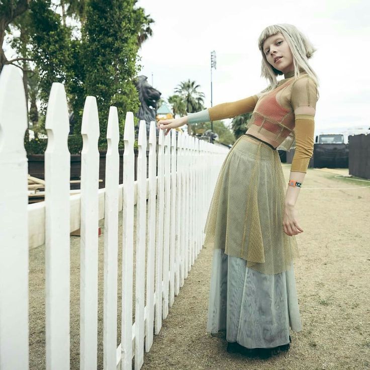 a woman leaning against a white fence with her hand on the top of one leg