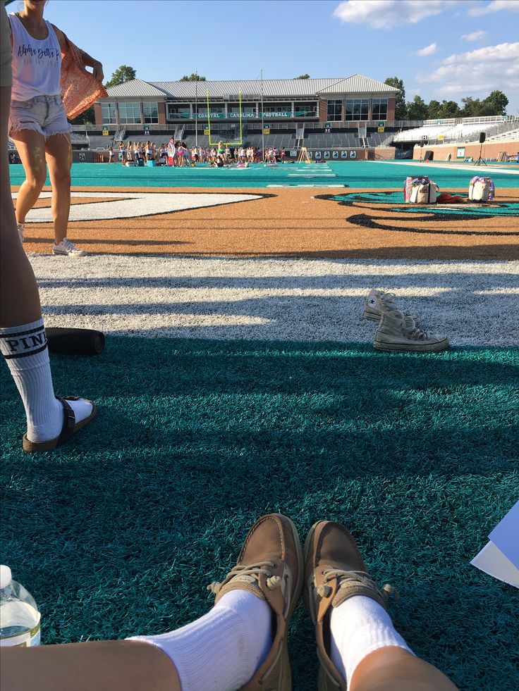 two people with their feet up on the ground in front of an empty baseball field