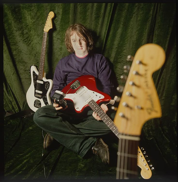 a man sitting in front of three guitars