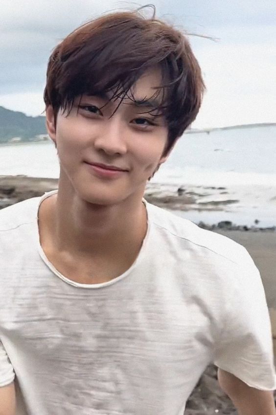 a young man standing on top of a beach next to the ocean with his hand in his pocket