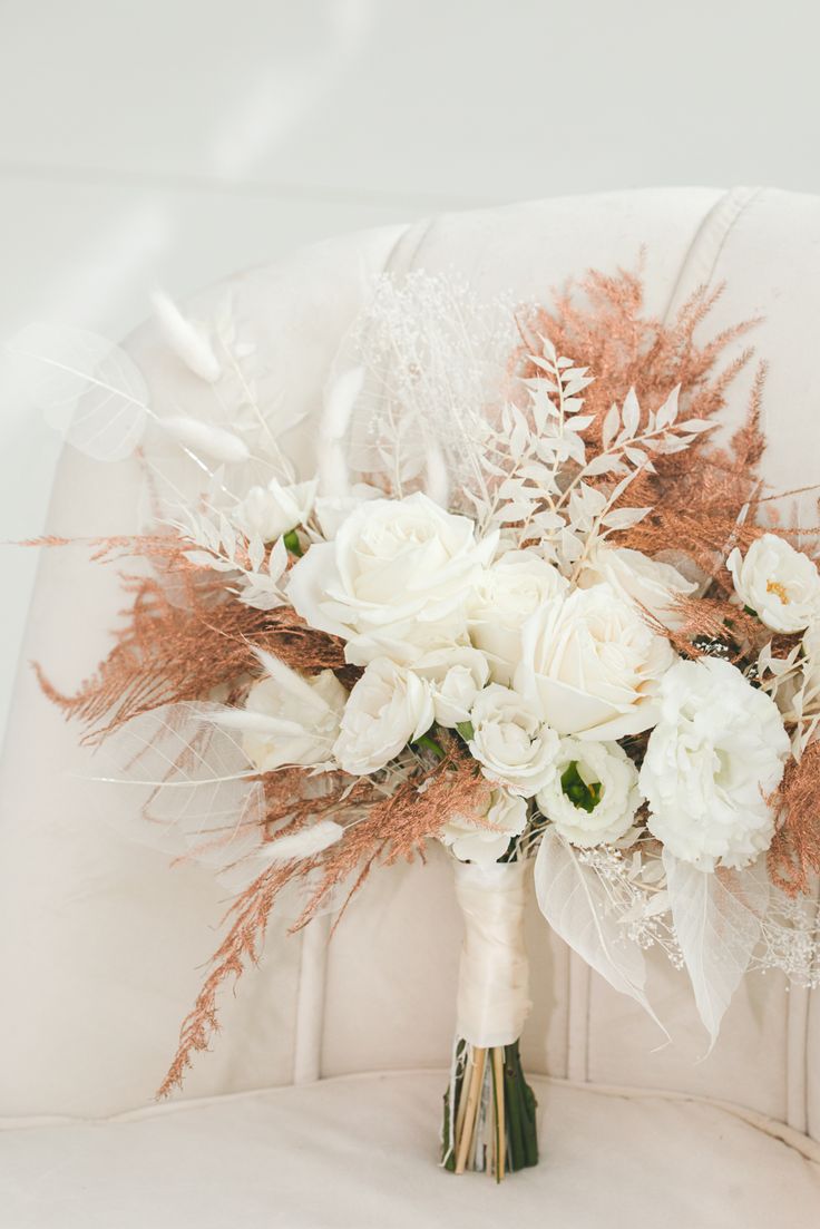 a bridal bouquet sitting on top of a white chair with feathers and flowers in it