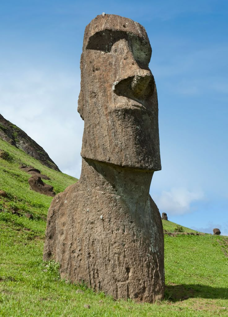 a large stone statue sitting on top of a lush green hillside under a blue cloudy sky